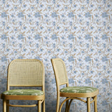 Two wicker chairs with green cushions against a blue and brown floral wallpapered wall.