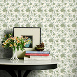 Decorative table with books and a vase against a sage green floral wallpapered wall.