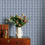 Vintage wooden dresser with a vase of flowers against a blue floral patterned wallpaper.