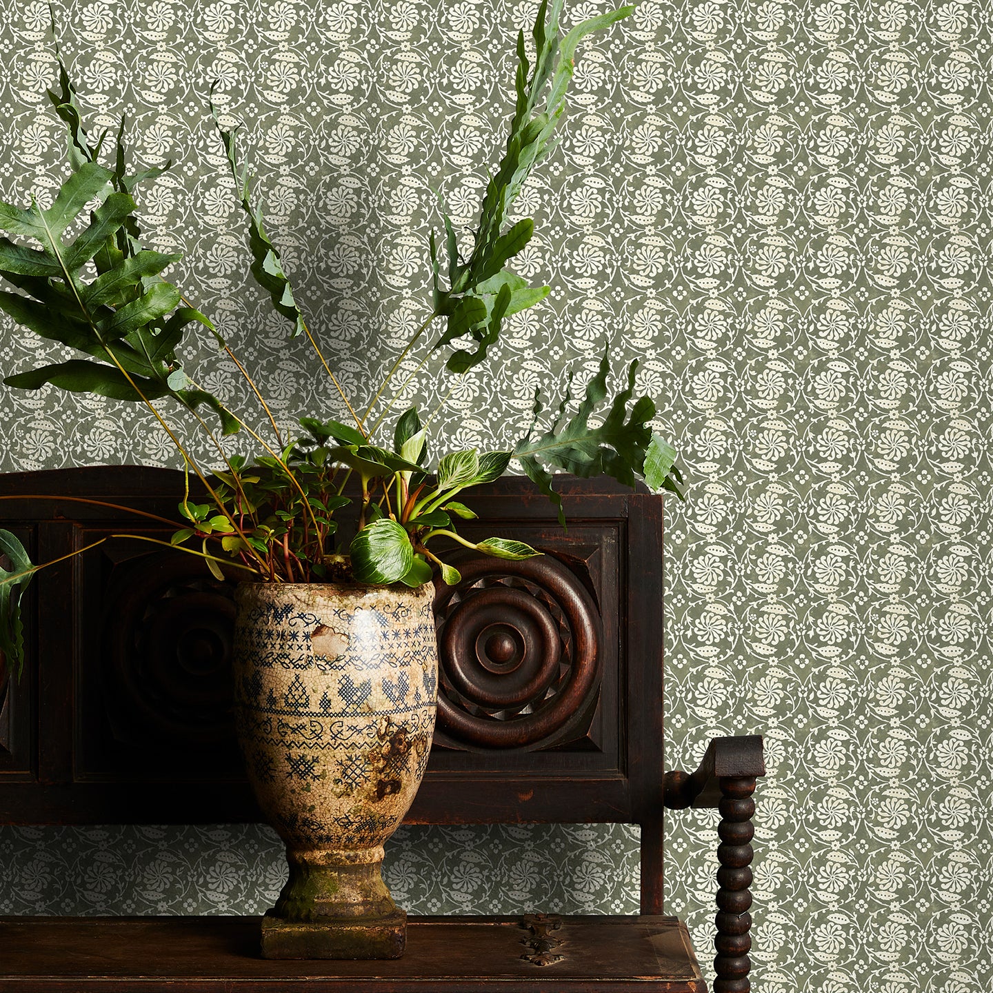 Decorative green floral wallpaper with a subtle pattern, potted plant on a wooden cabinet.