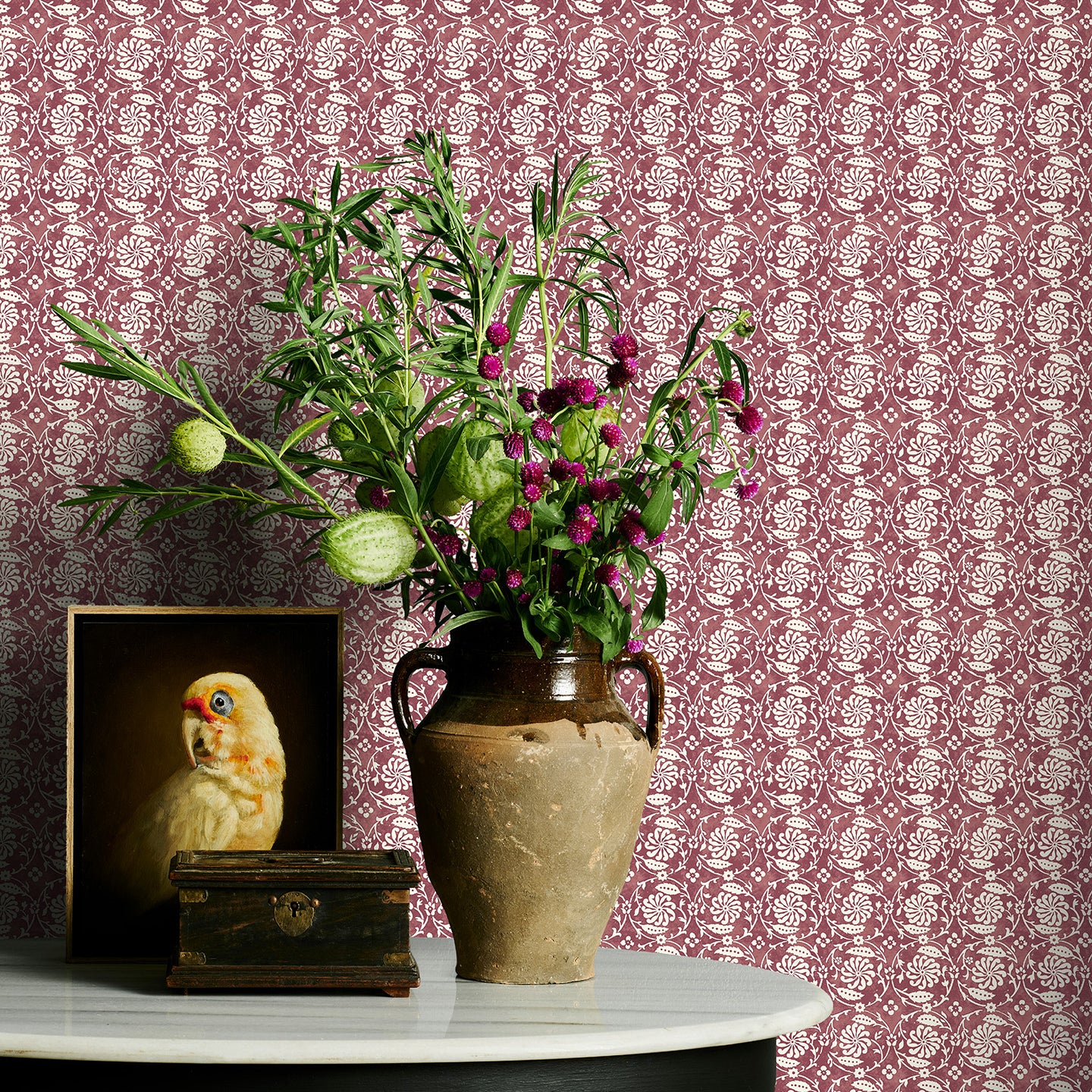 Decorative table with vase of flowers and owl figurine against a wine floral patterned wall.
