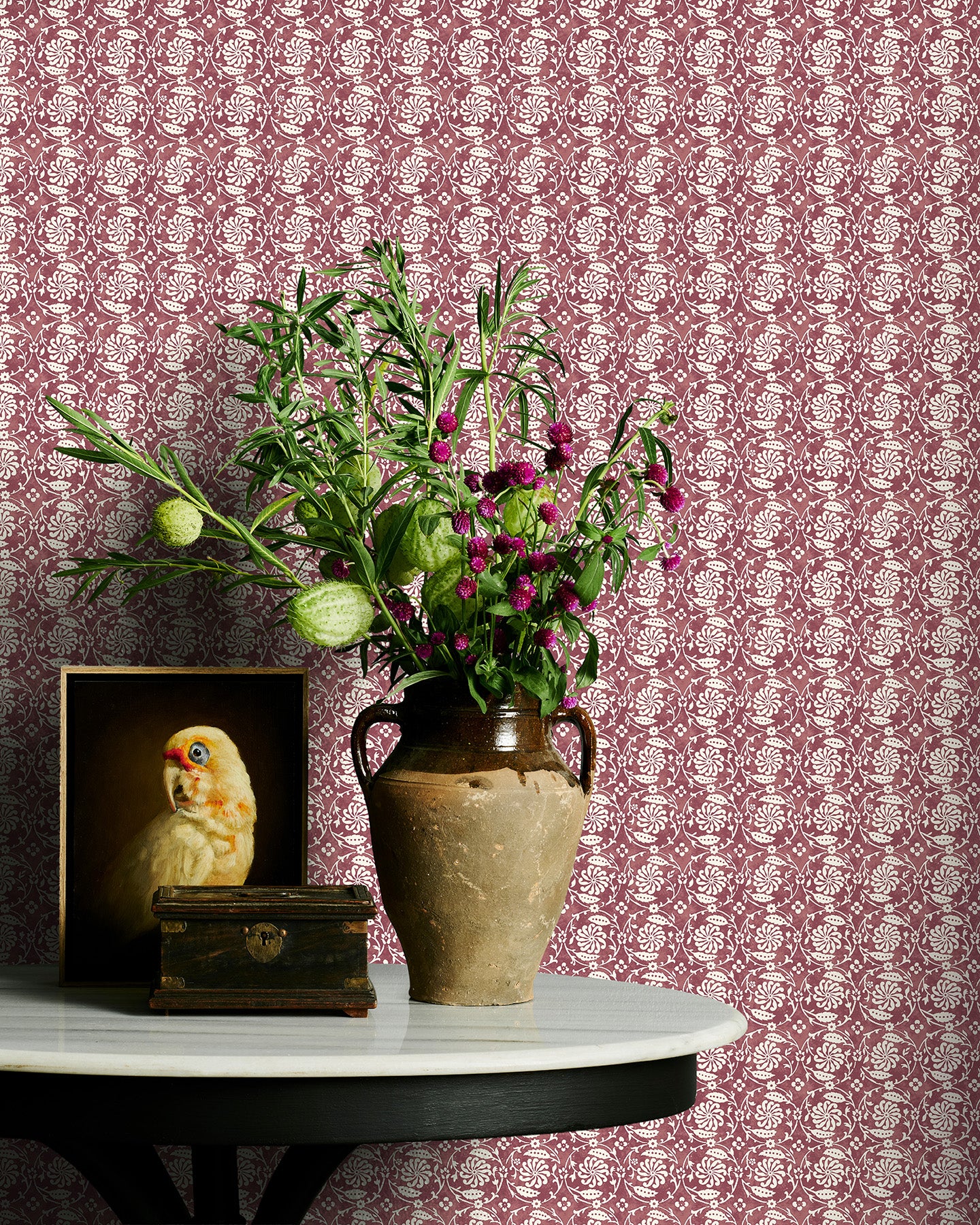 Decorative table with vase of flowers and owl figurine against a wine floral patterned wall.