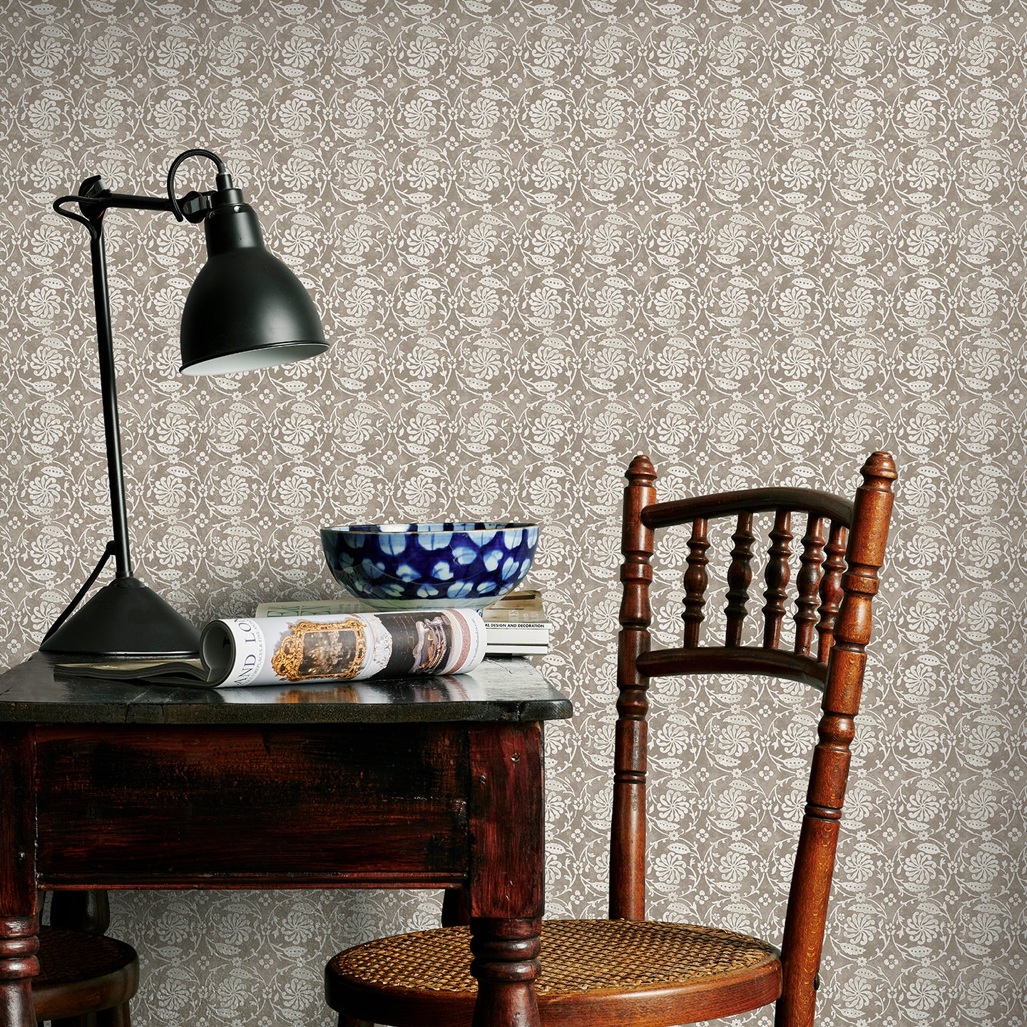 Room interior with wooden table, chair, and lamp against a brown floral patterned wall.