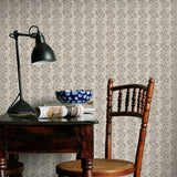 Room interior with wooden table, chair, and lamp against a brown floral patterned wall.