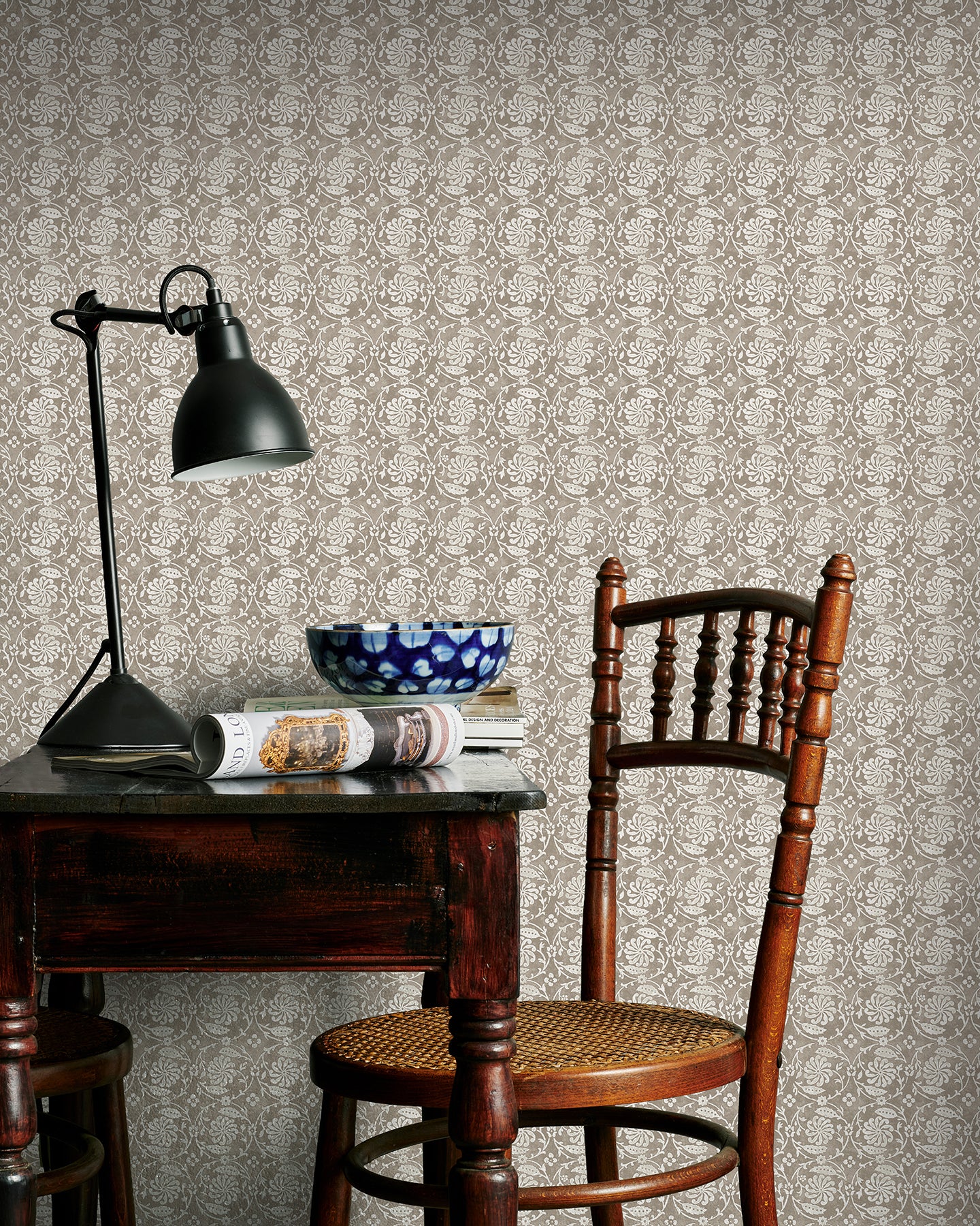 Room interior with wooden table, chair, and lamp against a brown floral patterned wall.