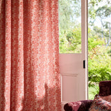 Upholstered red chair with pink patterned fabric curtain against an open door leading to the garden