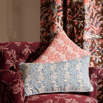 Decorative pillows on a floral-patterned armchair with floral-fauna printed curtains.