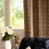 Decorative curtain with floral pattern in a room with a window and a vase of flowers on a table.