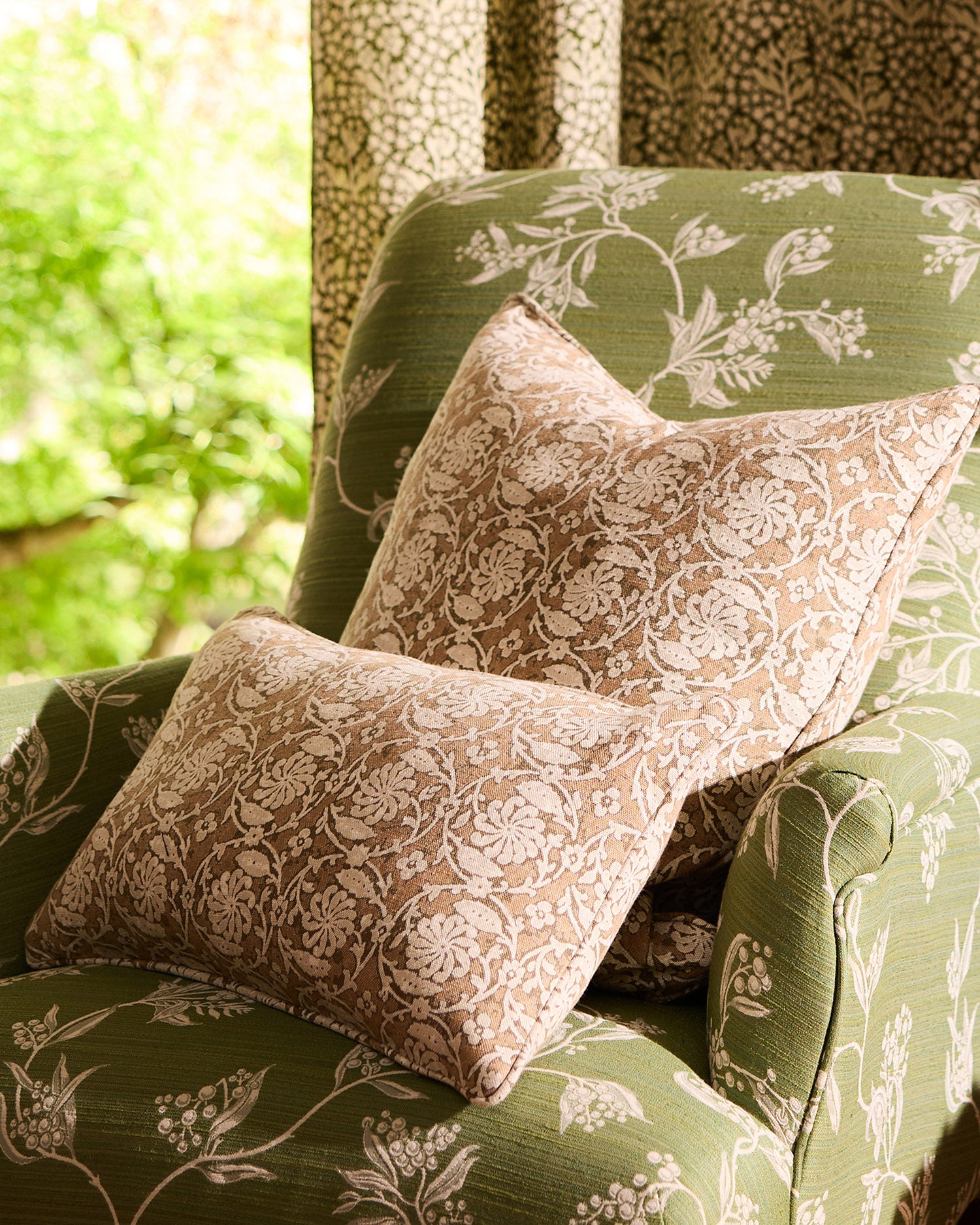 Floral-patterned cushions on a green upholstered chair with a blurred outdoor background