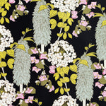 Detail of wallpaper in a dense floral print in pink, green and yellow on a black field.
