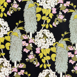 Detail of wallpaper in a dense floral print in pink, green and yellow on a black field.