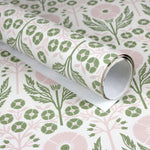 Wallpaper roll in an arts and crafts style floral pattern in pink and green on white. 