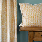 Patterned pillow on a wooden bench against a teal wall with curtains.