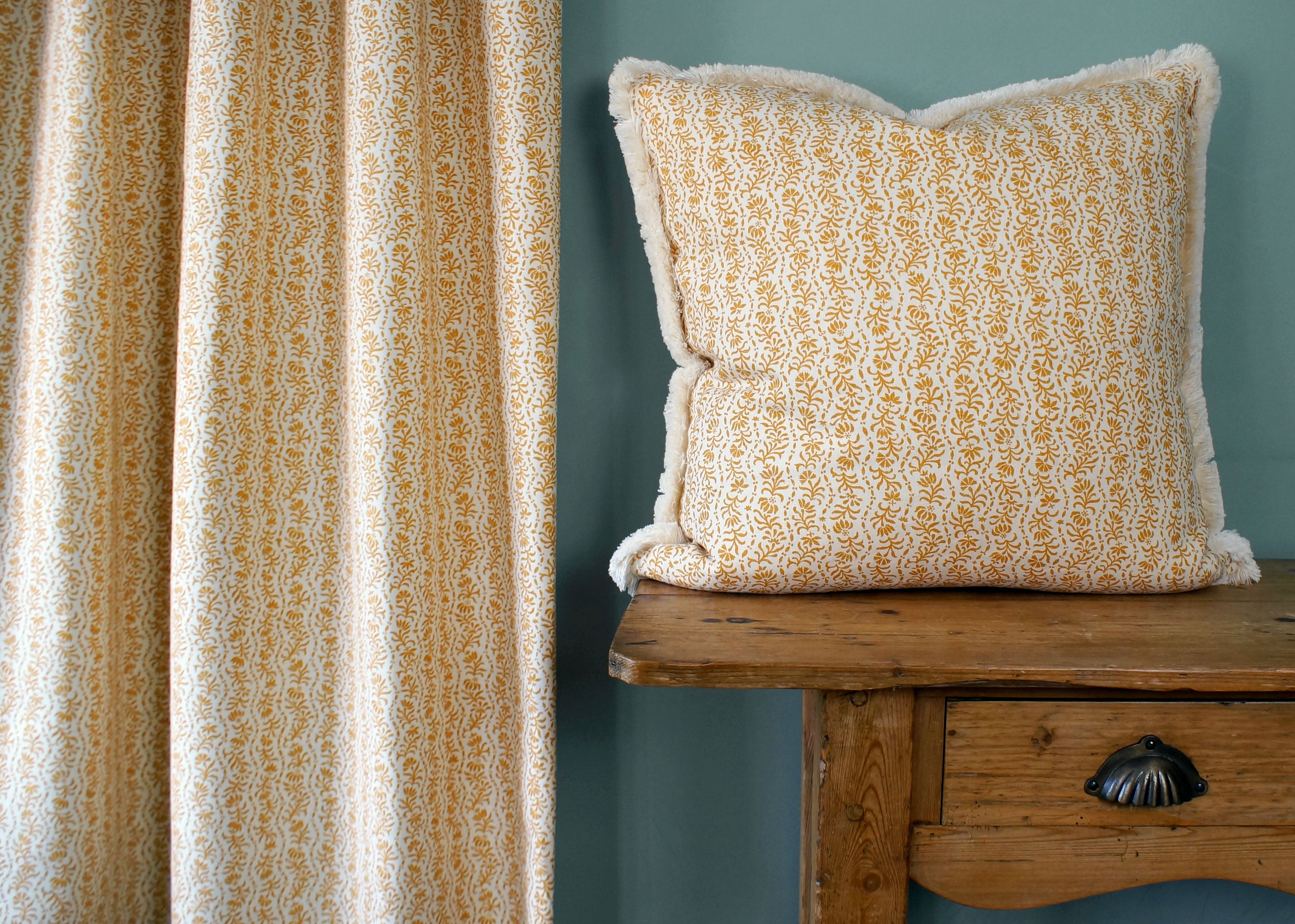 Patterned pillow on a wooden bench against a teal wall with curtains.
