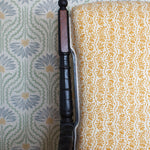 Wooden chair with a yellow floral fabric against wallpaper in a pastel floral pattern.