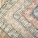 Stack of broadloom carpet samples in a textural herringbone design in a range of colors. 