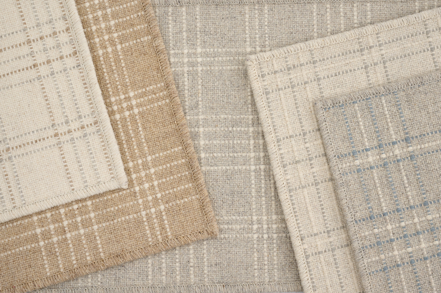 Stack of broadloom carpets in a windowpane plaid pattern in various light neutral colors. 