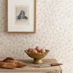 Detail of a styled interior scene set against wallpaper in beige watercolor animal patter with a framed abstract charcoal sketch with a rustic wooden table with two baguettes, footed ceramic bowl with brown eggs, serving fork and knife.