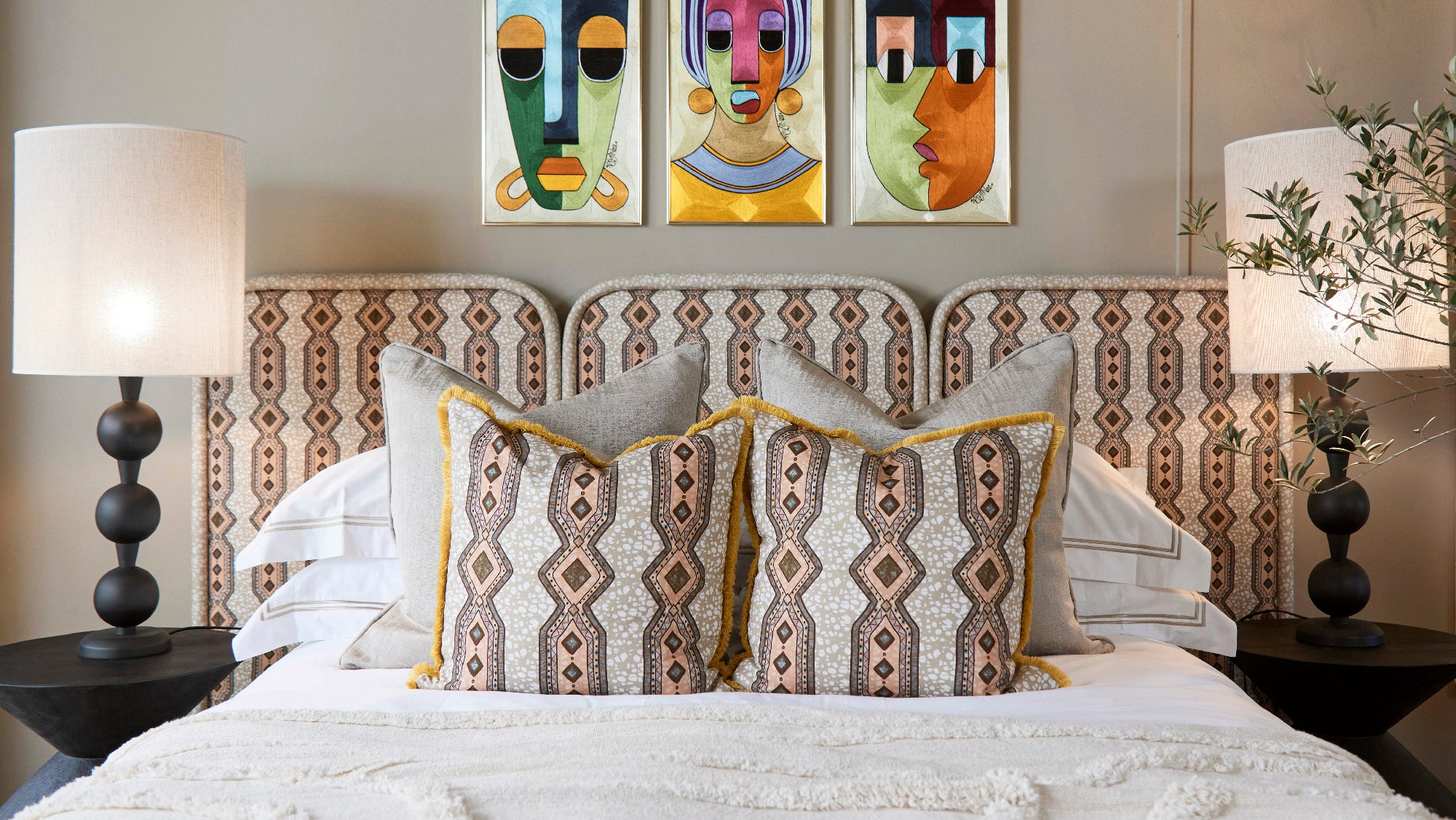 Bedroom scene with decorative pillows and headboard in a light coral and tan geometric stripe fabric. 