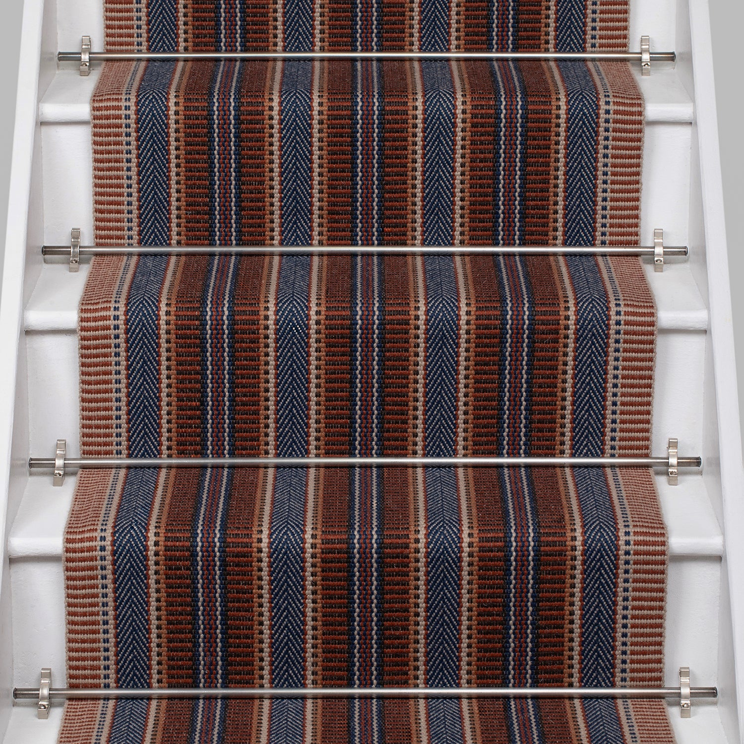 White stair case with a complex woven striped runner made of wool in shades of blue and red. 