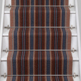 White stair case with a complex woven striped runner made of wool in shades of blue and red. 