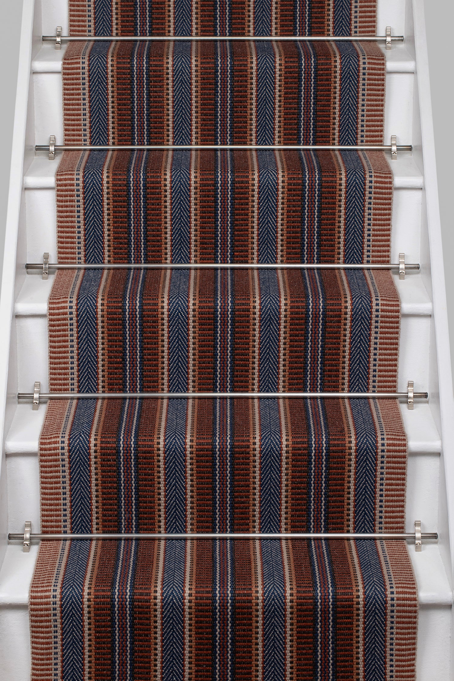 White stair case with a complex woven striped runner made of wool in shades of blue and red. 