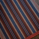 Detail of an area rug on a wood floor in a complex woven stripe made of wool in shades of blue and red. 