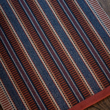 Detail of an area rug on a wood floor in a complex woven stripe made of wool in shades of blue and red. 