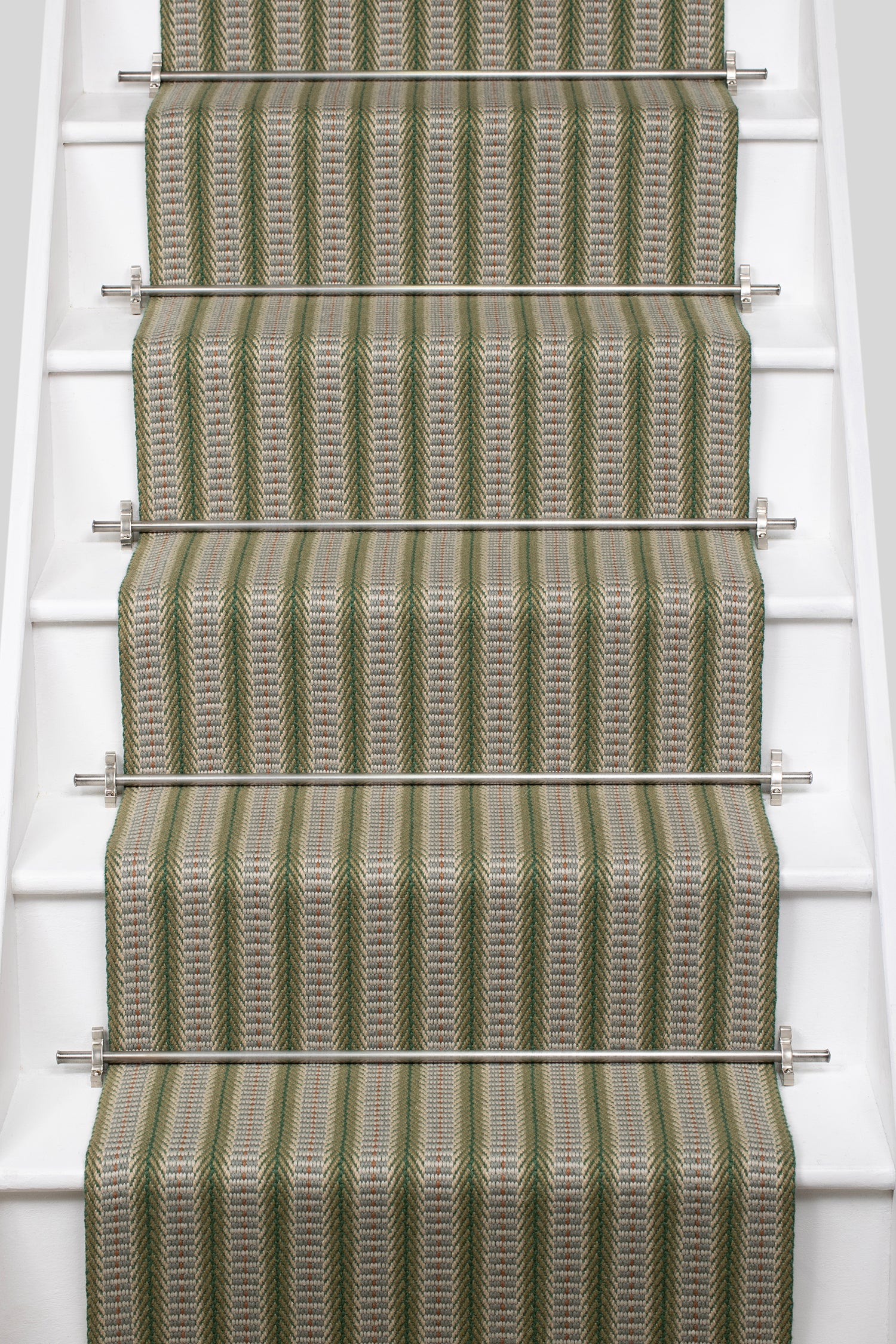 White stair case with a complex woven striped runner made of wool in shades of green with grey and red accents.