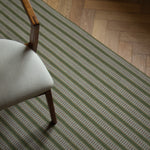 Detail of an area rug in a complex woven striped runner made of wool in shades of green with grey and red accents on a wood parquet floor.