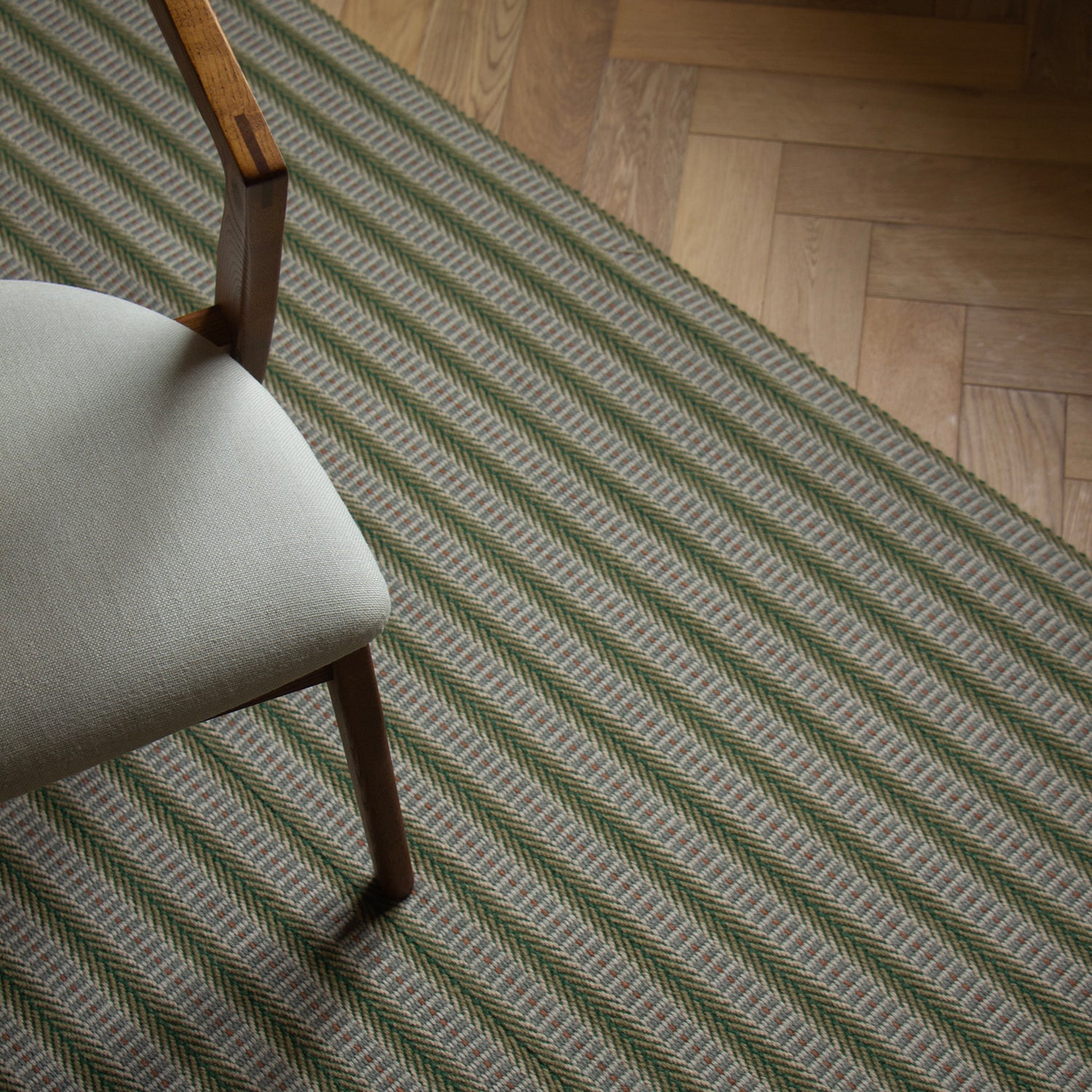 Detail of an area rug in a complex woven striped runner made of wool in shades of green with grey and red accents on a wood parquet floor.