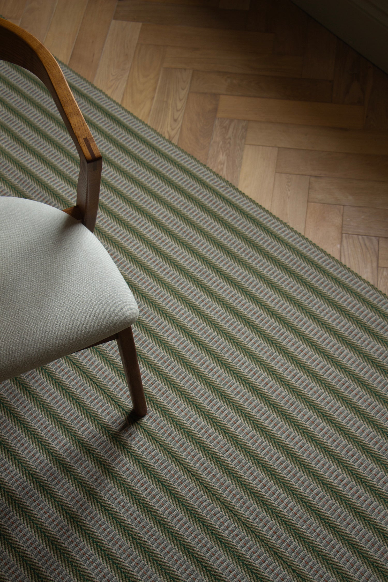Detail of an area rug in a complex woven striped runner made of wool in shades of green with grey and red accents on a wood parquet floor.