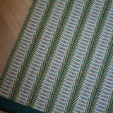 Detail of an area rug in a complex woven striped runner made of wool in shades of green with grey and red accents on a wood floor.
