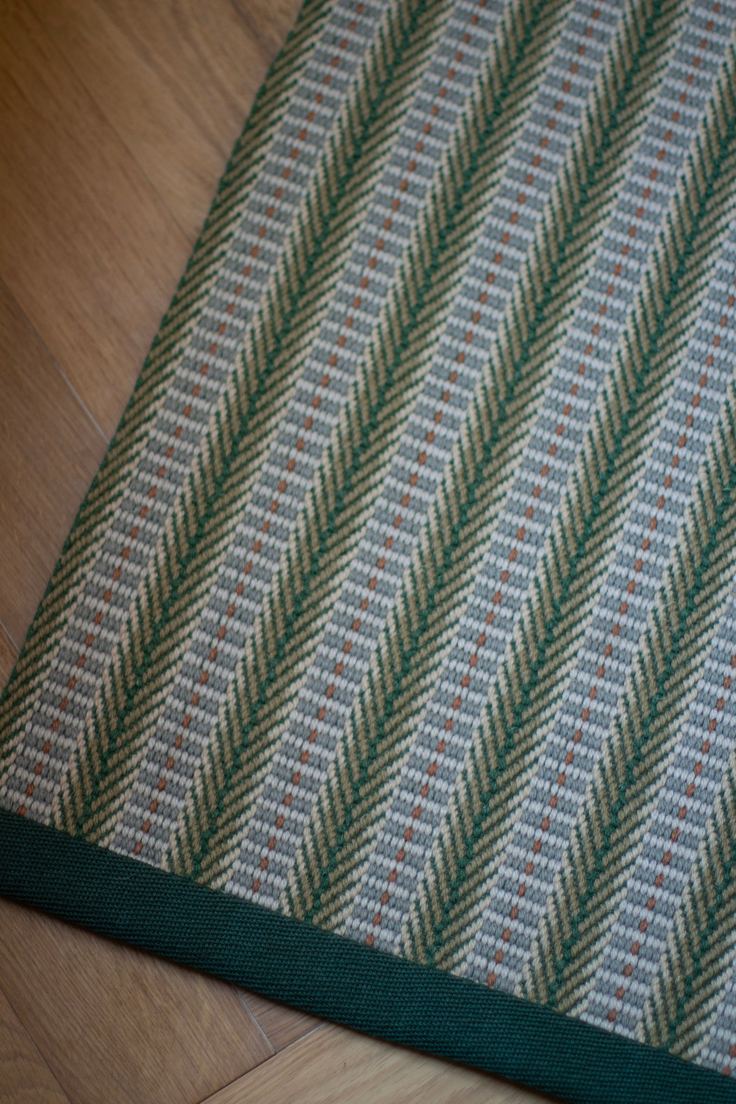 Detail of an area rug in a complex woven striped runner made of wool in shades of green with grey and red accents on a wood floor.
