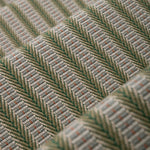 Detail of an stair runner in a complex woven striped runner made of wool in shades of green with grey and red accents on a wood parquet floor.