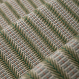 Detail of an stair runner in a complex woven striped runner made of wool in shades of green with grey and red accents on a wood parquet floor.