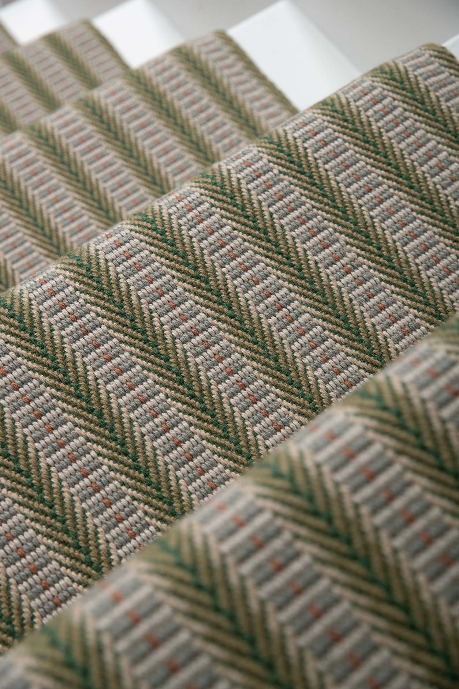 Detail of an stair runner in a complex woven striped runner made of wool in shades of green with grey and red accents on a wood parquet floor.