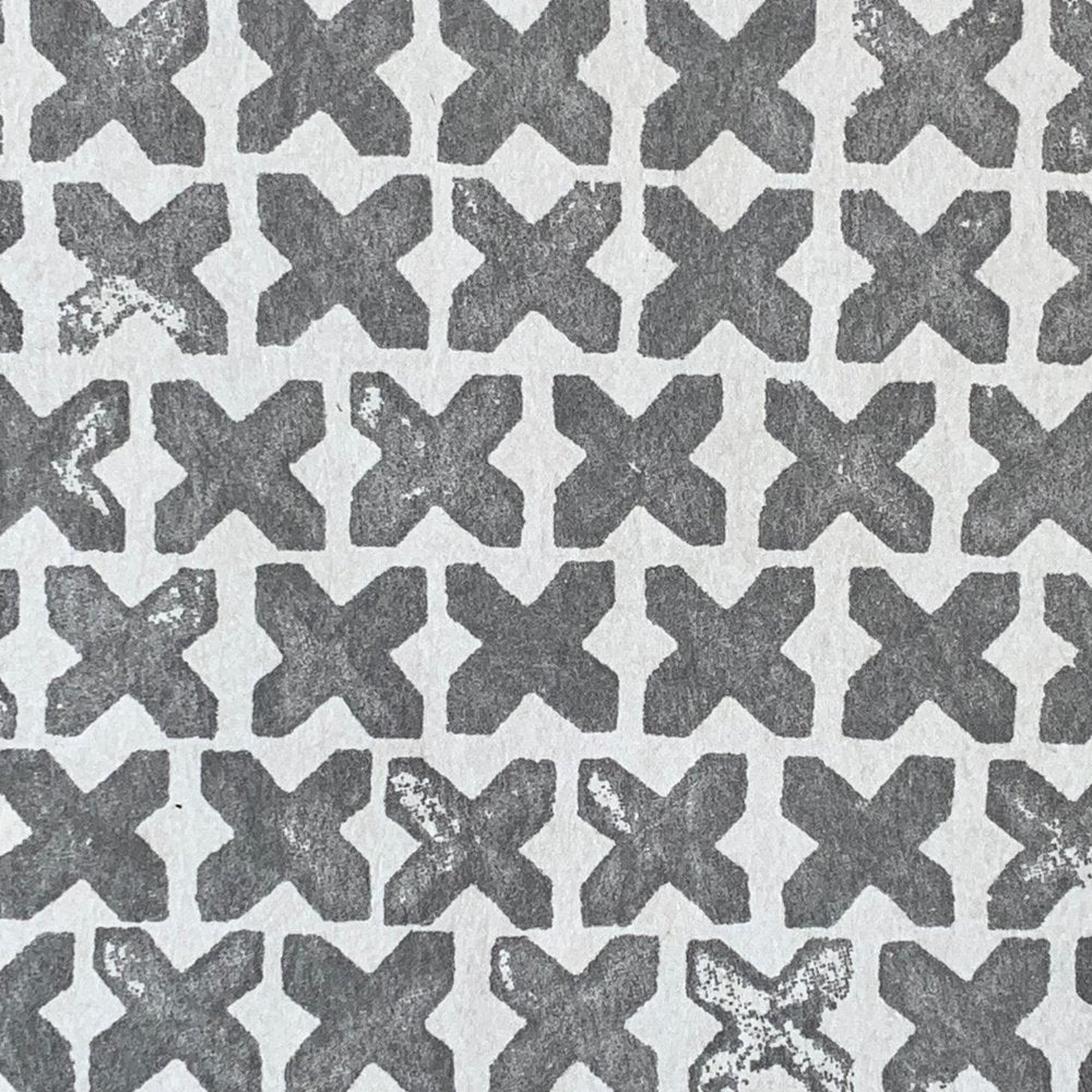 Close-up of wallpaper in a repeating "X" print in gray on a white field.