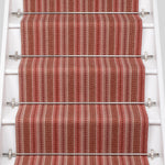 White staircase with a runner in a complex woven striped runner made of wool in shades of red.
