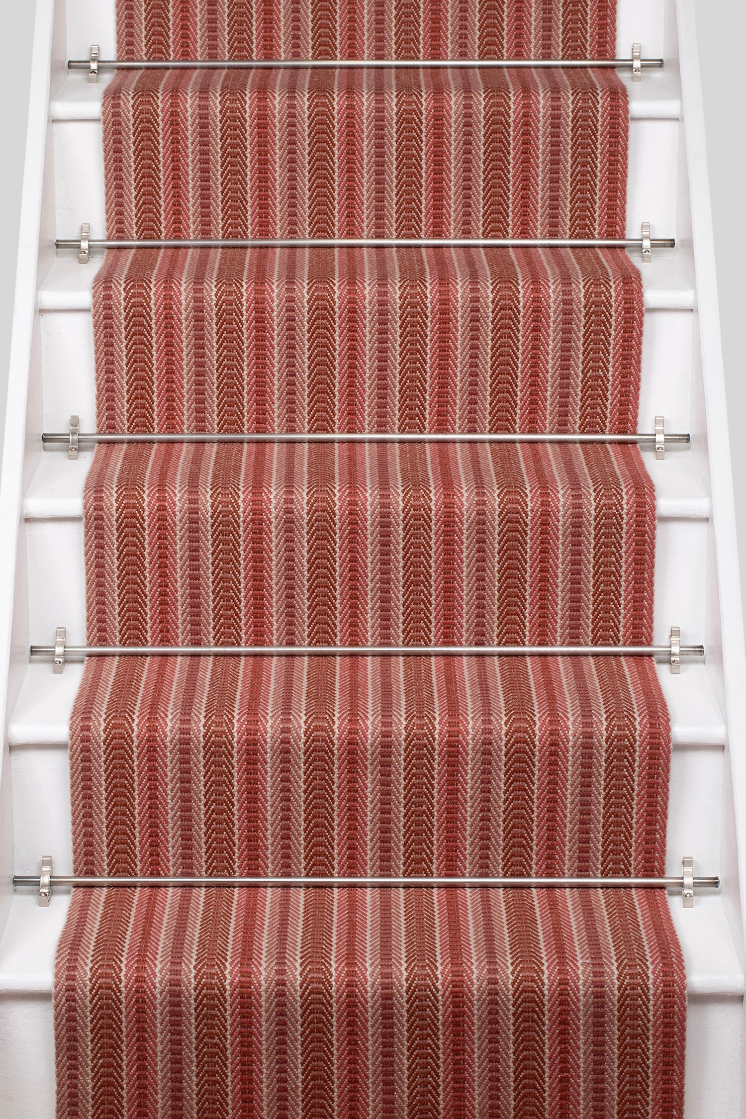 White staircase with a runner in a complex woven striped runner made of wool in shades of red.
