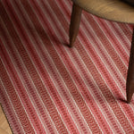 Detail of an area rug in a complex woven striped runner made of wool in shades of red.