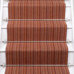 A close-up view of a staircase with carpeted steps in a red-orange stripe pattern, bordered by white risers.
