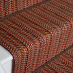 Close-up of a carpeted staircase with a textured herringbone pattern in rust orange, brown.
