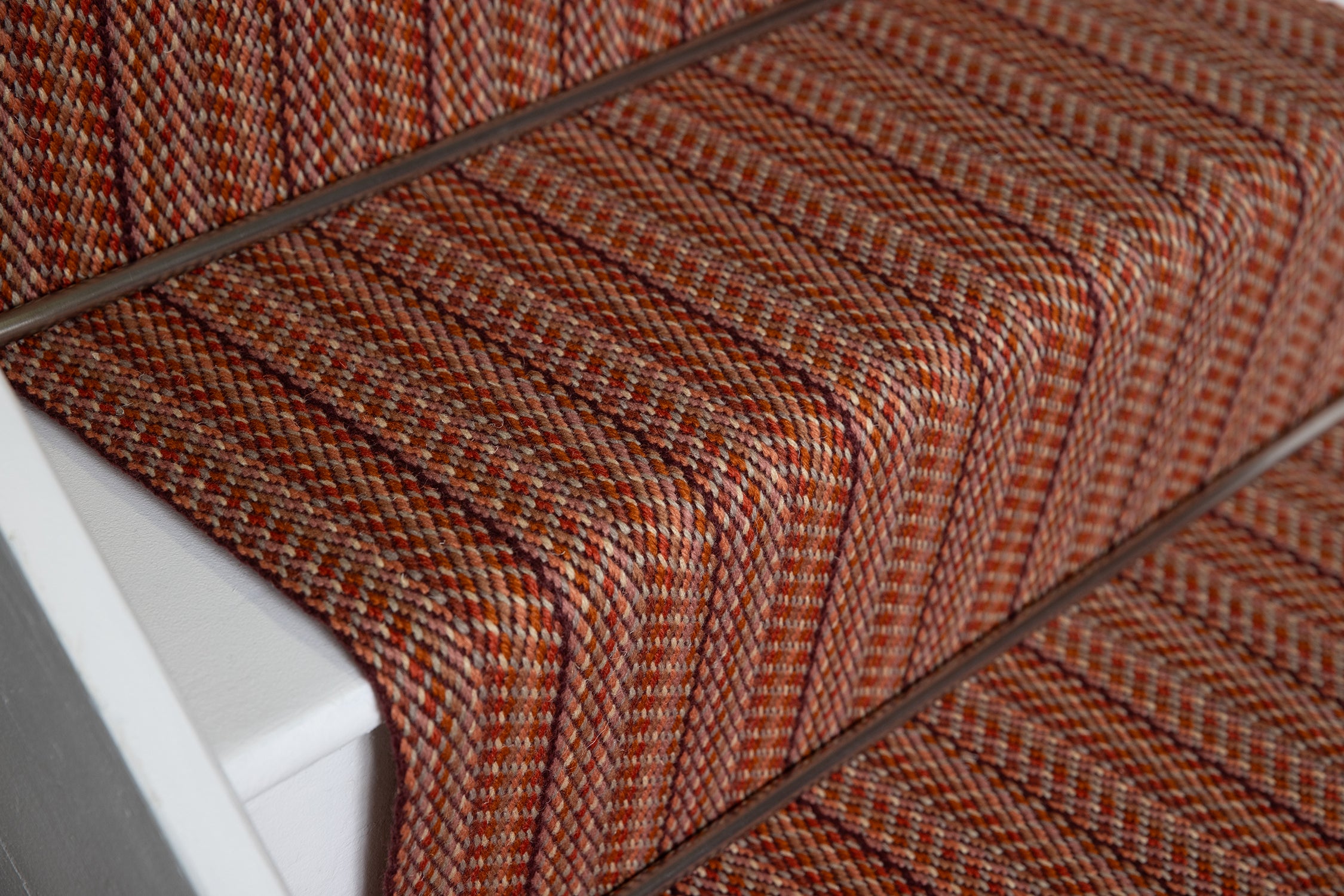 Close-up of a carpeted staircase with a textured herringbone pattern in rust orange, brown.