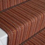 Close-up of a carpeted staircase with a textured herringbone pattern in rust orange, brown.