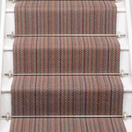 A close-up view of a staircase with carpeted steps in a pink-brown-blue stripe pattern, bordered by white risers