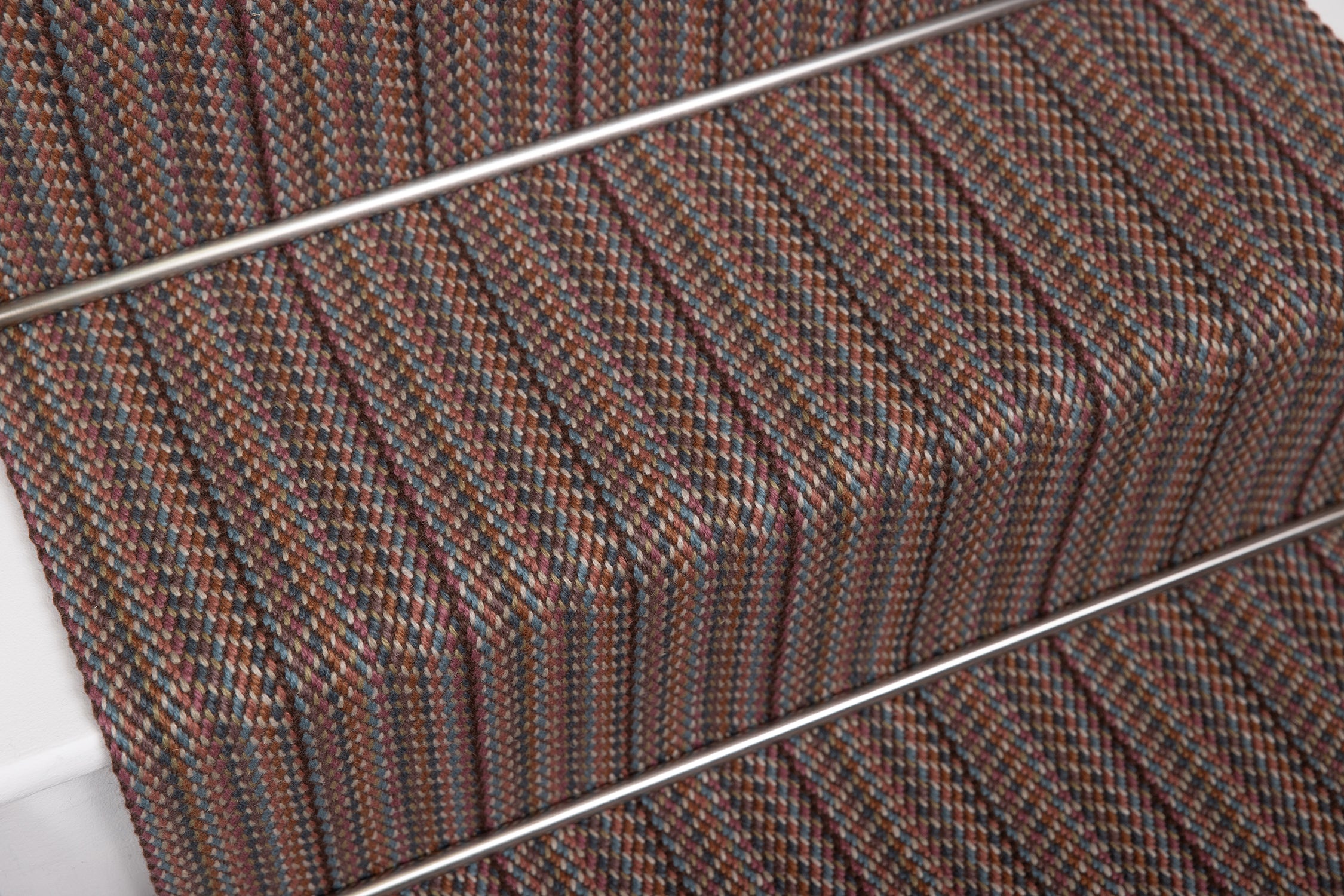 Close-up of a woven stair carpet runner with a textured stripe pattern in pink, brown, beige, and blue.