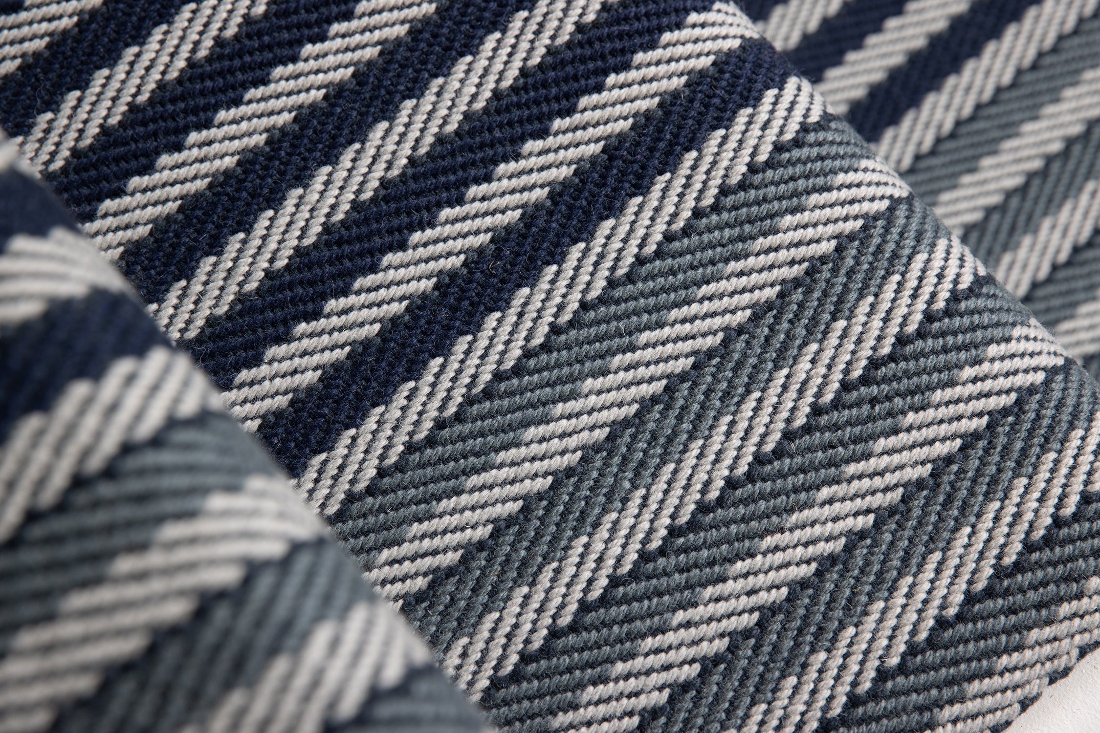 Close-up of a stair runner with a diagonal herringbone stripe in navy blue, steel blue and grey.