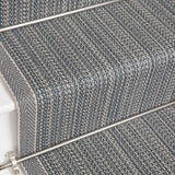 Close-up of carpeted stairs with a textured herringbone pattern in gray and blue tones, showing the stair treads and metal rail.