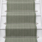 A textured stair runner in a muted sage green color installed on a white staircase, secured by silver metal rods.